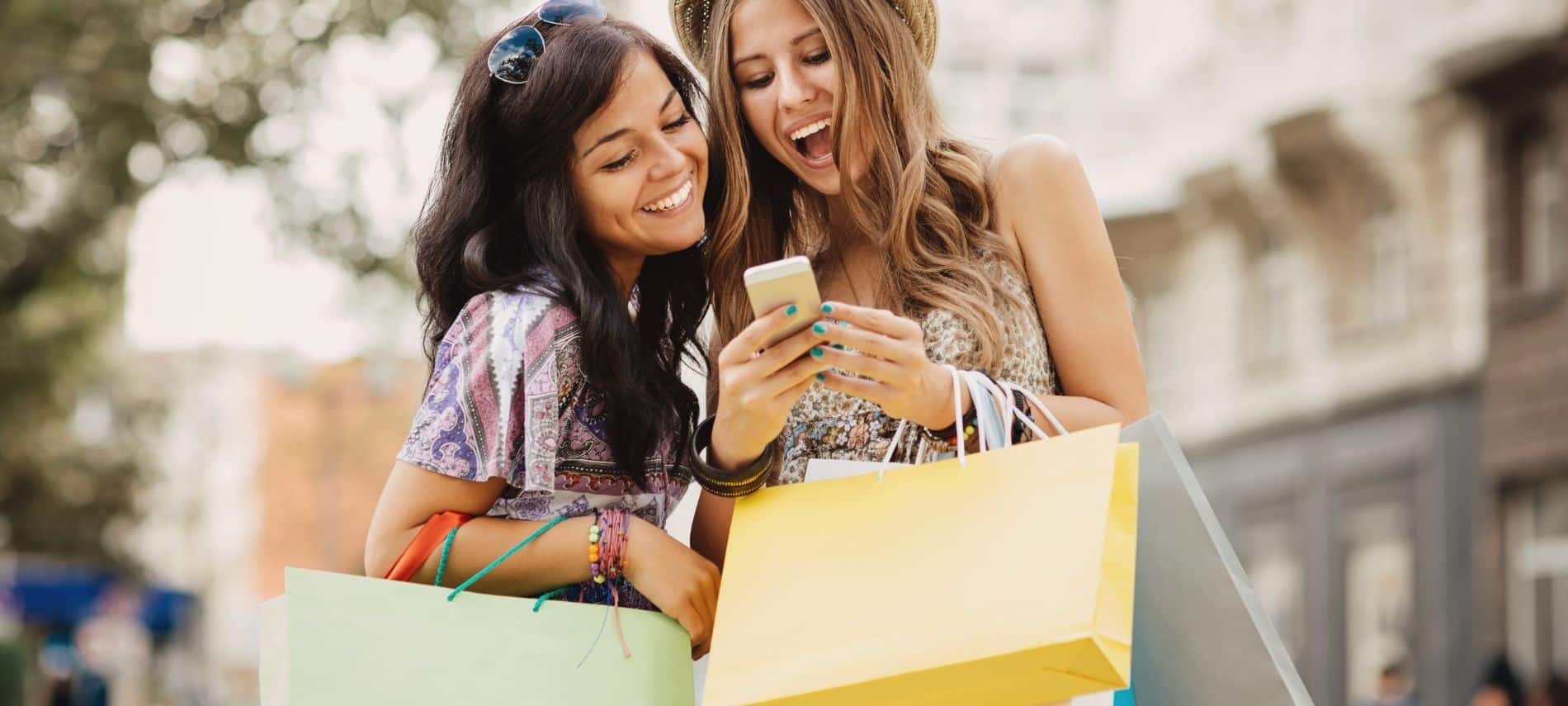 two women shopping and holding bags while looking at phone and smiling