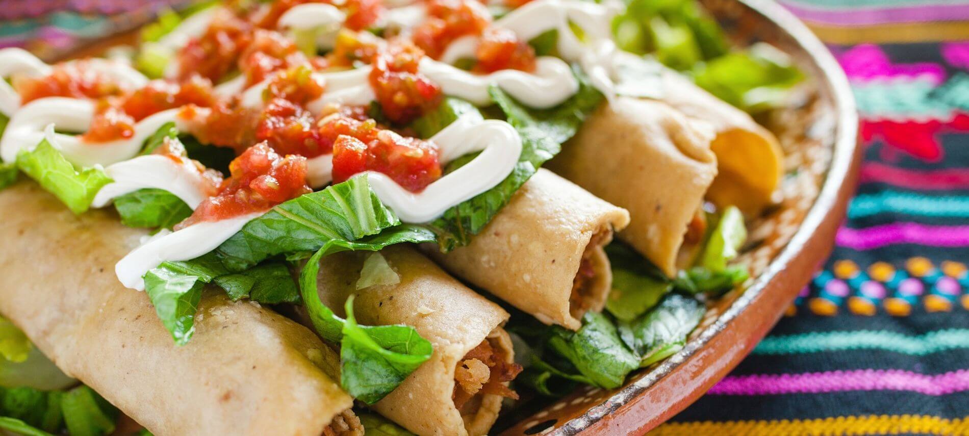 plate of flautas de pollo topped with homemade salsa on a mexican blanket