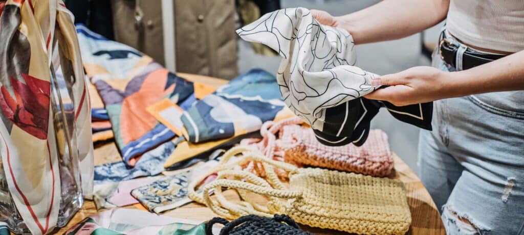 a person holding a vintage scarf in front of a table of vintage bags and scarves